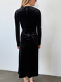 Image slightly cropped of behind view of woman wearing a black velvet dress with long sleeves against a white background