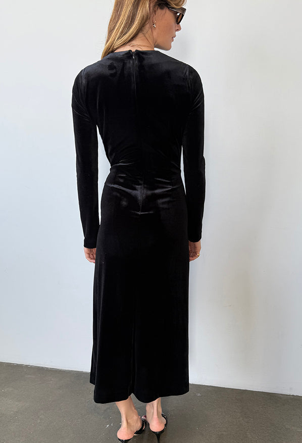 Image slightly cropped of behind view of woman wearing a black velvet dress with long sleeves against a white background