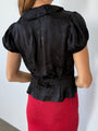 Cropped chin to thigh, back view of woman wearing a black floral patterned blouse with short sleeves and red sheer knit skirt against a white background