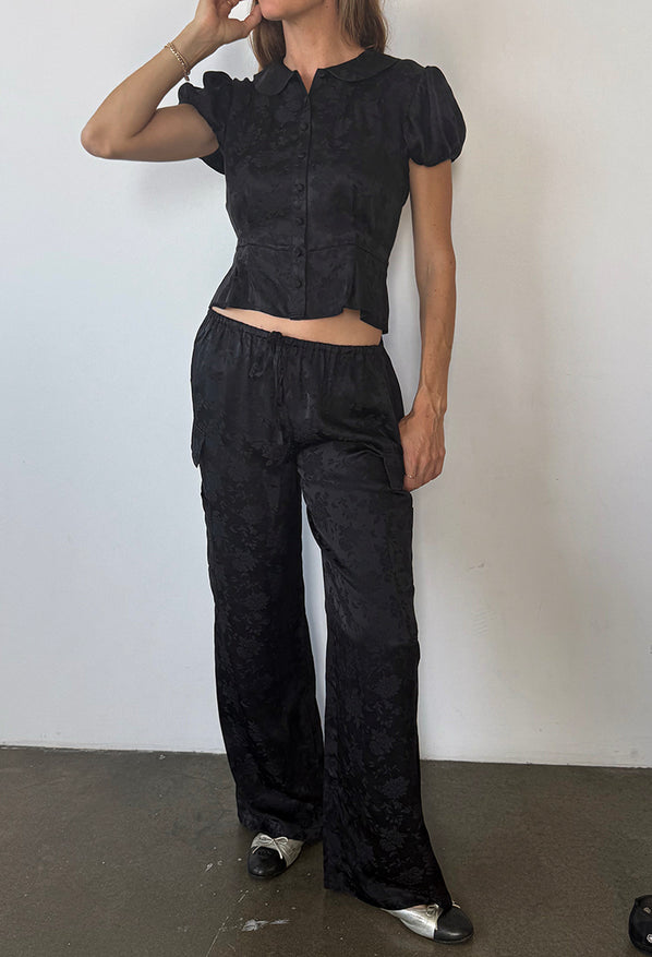 Image cropped chin down of woman wearing black floral patterned short sleeve top with matching pants against a white background