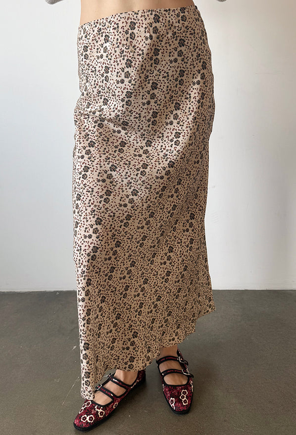 Cropped waist down of woman wearing a long silk and viscose skirt with floral cherry blossom pattern, and red floral shoes against a plain background