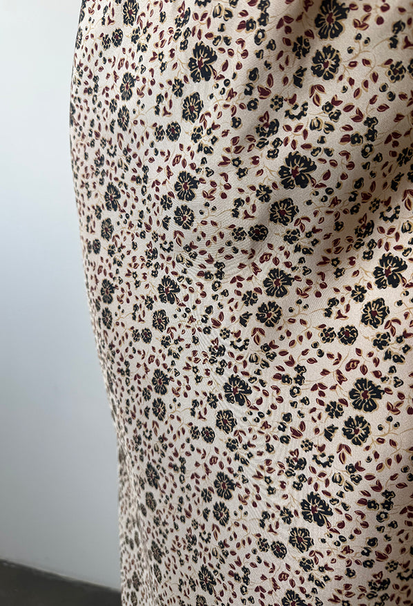 Cropped detail shot of a silky skirt with floral cherry blossom pattern against a plain background