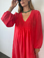 Cropped image of woman wearing a red caftan dress with long sleeves against a white background