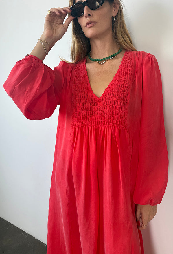 Cropped image of woman wearing a red caftan dress with long sleeves against a white background