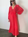 Slightly cropped image of woman wearing a red caftan dress against a white wall