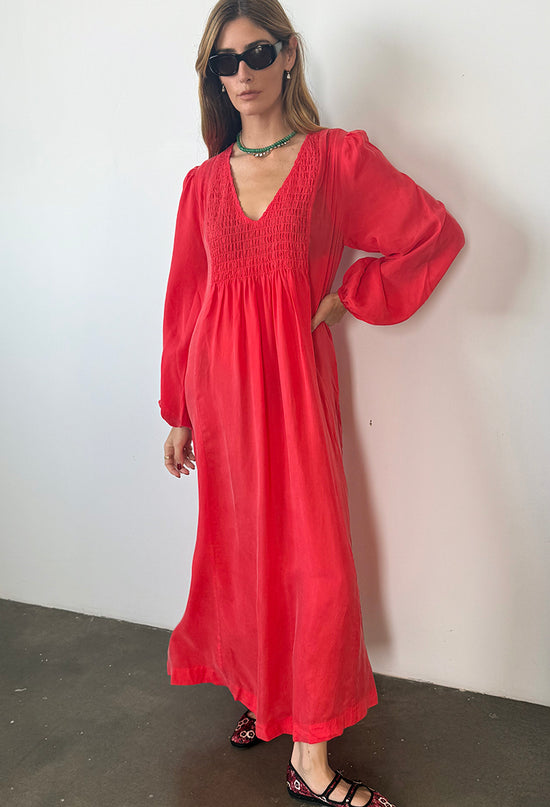 Slightly cropped image of woman wearing a red caftan dress against a white wall