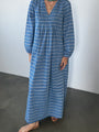 Cropped neck down of a woman in a long sleeve blue Caftan dress with a v-neck and zigzag print standing against a plain background.