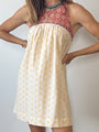 Image cropped neck to knees of woman wearing a mini length tank style shift dress with blood orange and white floral top and white skirt with yellow sun pattern against a white background. 