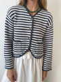 Cropped chin to thigh of woman wearing a striped white and navy knit cardigan with buttons against a white background. 