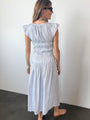 Back view of woman wearing a light blue pinstriped short-sleeved midi dress with smocking around the bust to the waist against a white wall