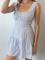 Cropped neck to knee of woman in a light blue pin-striped tank style mini dress with a smocked bodice against a plain background