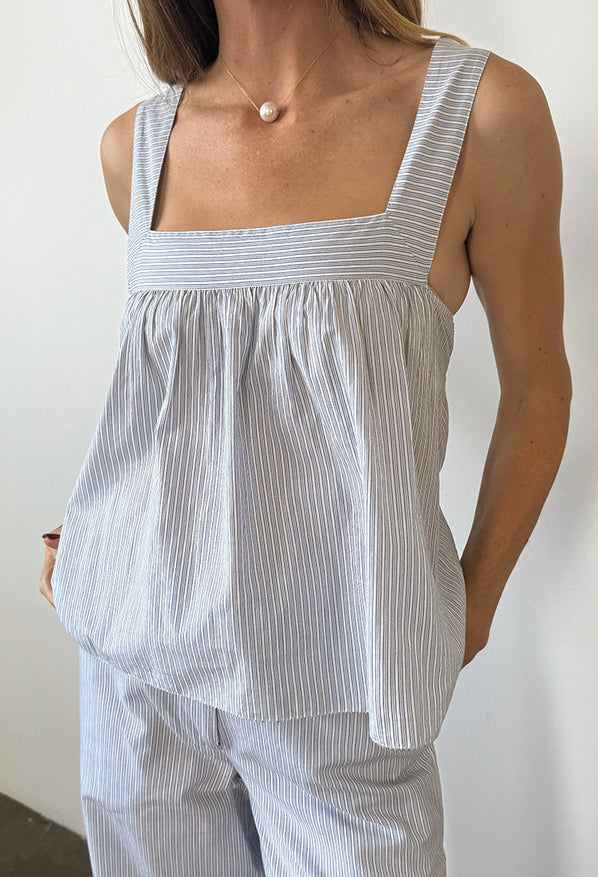 Cropped neck to thigh of woman in light blue pin-striped sleeveless top with matching wide-leg pants against a plain background. 