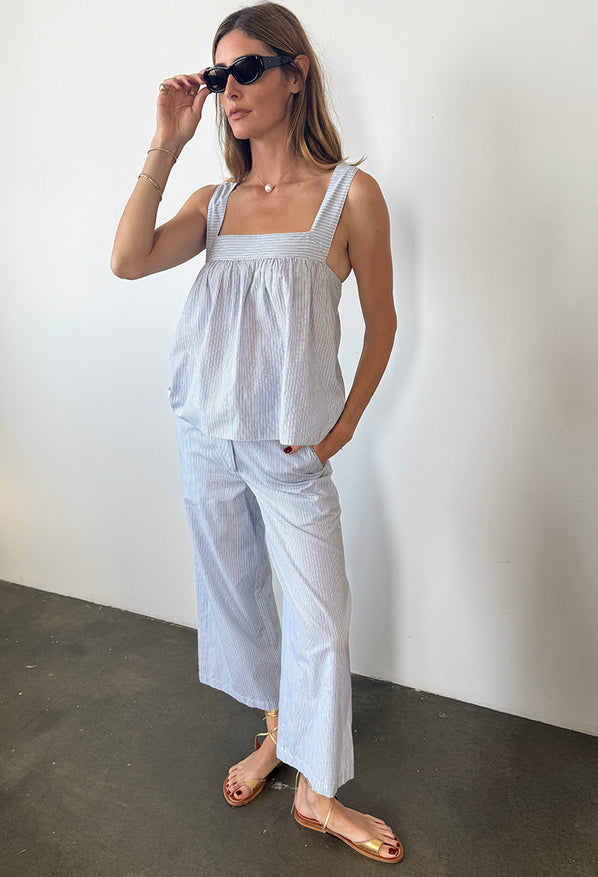 Woman in light blue pin-striped sleeveless top and matching wide-leg pants standing in front of a plain background. 