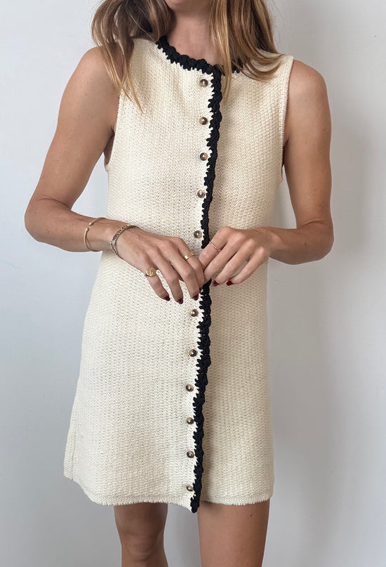 Cropped chin to knee of woman wearing an ivory button down dress with a round neckline and black trim details on a white background