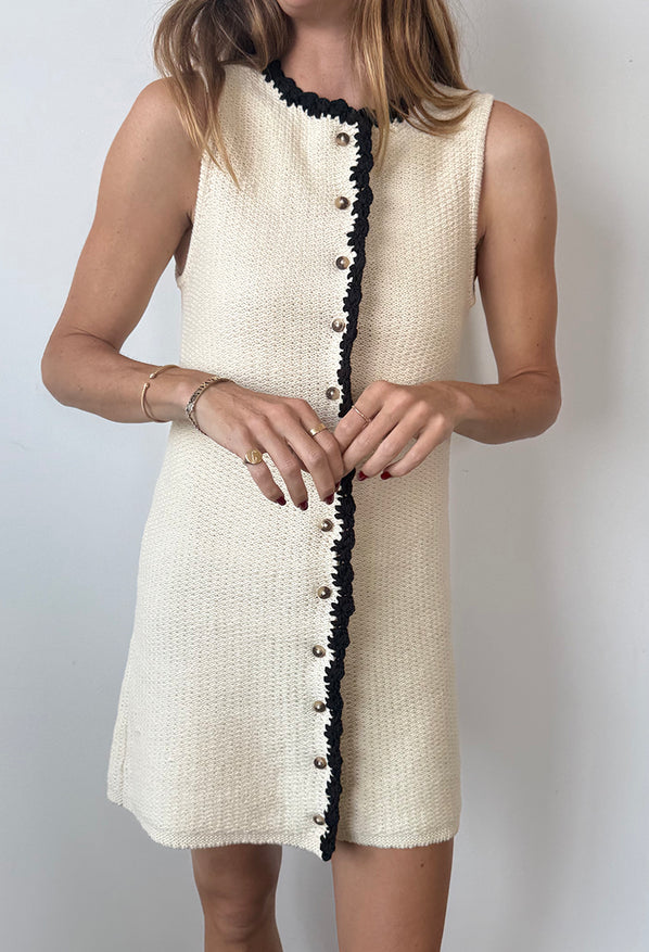 Cropped chin to knee of woman wearing an ivory button down dress with a round neckline and black trim details on a white background