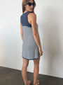 Back view of woman in a striped white and navy tank style knit dress against a plain background