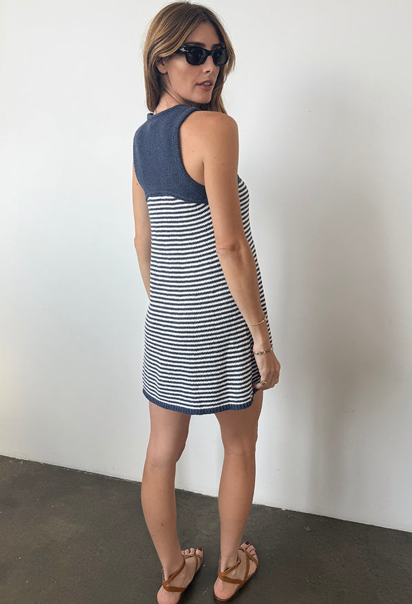 Back view of woman in a striped white and navy tank style knit dress against a plain background