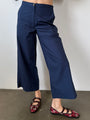Cropped waist down of woman wearing navy blue wide-leg pants with a plain background