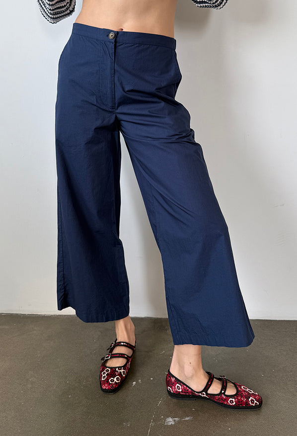 Cropped waist down of woman wearing navy blue wide-leg pants with a plain background