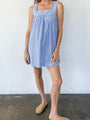 Woman wearing a light blue short dress against a white wall.
