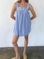 Woman wearing a blue striped short tank style dress against a white wall.