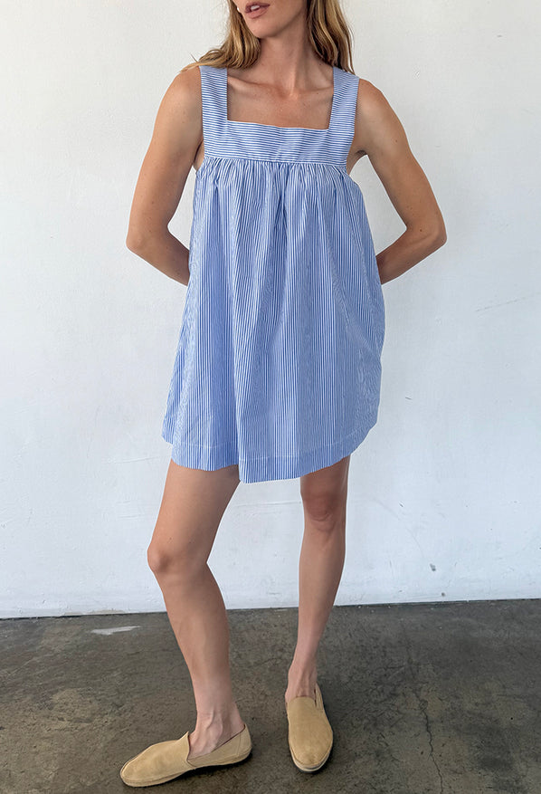 Woman wearing a blue striped short tank style dress against a white wall.