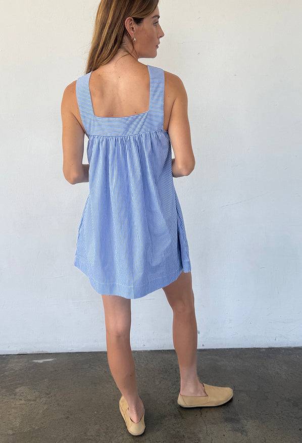 Back view of woman wearing a blue striped short tank style dress against a white wall.